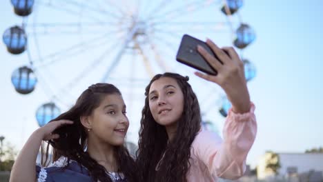 Zwei-schöne-Freundinnen-machen-eine-Selfie-im-Hintergrund-von-einem-Riesenrad.-4-K.-Nahaufnahme