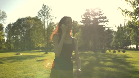 Smiling-young-attractive-female-walking-at-the-park-outdoors-talking-by-phone