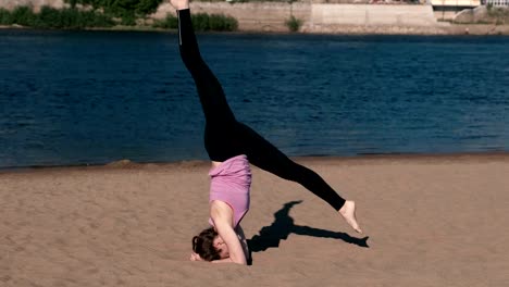 Mujer-haciendo-yoga-en-la-playa-por-el-río-en-la-ciudad.-Hermosa-vista.-Handstand.-La-guita-en-el-aire.-De-alta-velocidad.