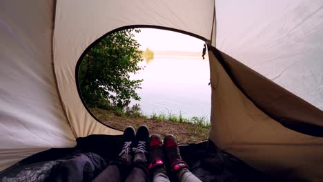 Turistas-en-tienda-mover-pies-haciendo-movimientos-de-danza-diversión-relajante,-hermosa-vista-del-lago-o-río-es-fuera.-Personas,-naturaleza-y-concepto-de-camping.