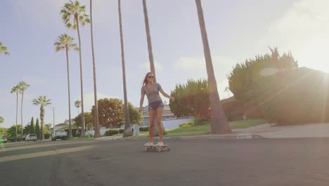 Attractive-adventurous-girl-skateboarding-down-palm-tree-lined-street-at-sunset