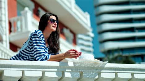 Elegante-mujer-Europea-en-gafas-de-sol-en-la-terraza,-apoyado-en-la-barandilla-antiguo-disfrutando-de-sol