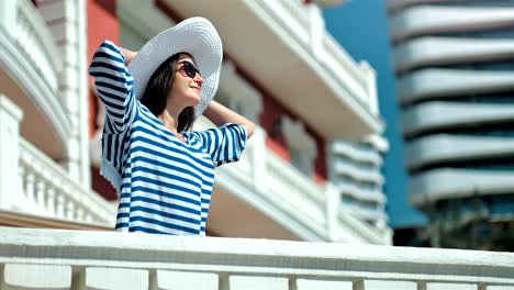 Glamour-young-woman-having-good-time-outdoor-raising-hands-and-holding-hat-on-her-head-enjoying-sun