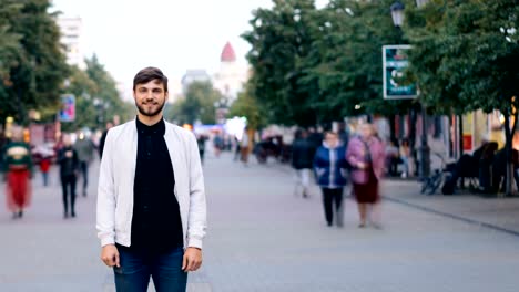 Zeitraffer-der-zuversichtlich-Mann-in-Jeans-und-weiße-Jacke,-in-der-Straße-in-der-Stadt-und-Blick-in-die-Kamera,-während-Leute-an-Herbsttag-durch-Rauschen-sind-allein-stehend.