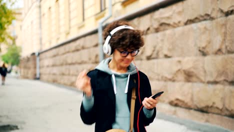 Gut-aussehende-Brünette-in-stilvollen-Gläsern-ist-Radio-im-Kopfhörer-hören-und-mit-Smartphone-beim-Spaziergang-in-Modent-Stadt-im-Herbst.-Menschen-und-urban-Life-Konzept.