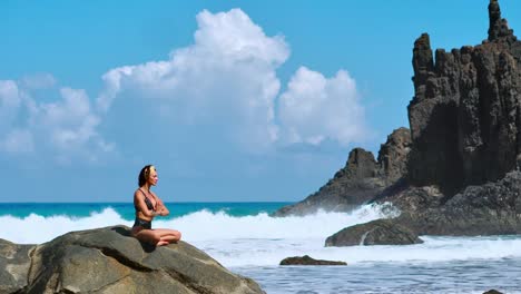 Ruhige-Meditation-Yoga.-Brünette-touristischen-Frau-meditieren-im-Lotussitz-auf-Felsvorsprung-über-dem-malerischen-Praia-da-Marinha.-Meditieren-Weibchen-auf-den-Klippen-der-Kanarischen-Inseln