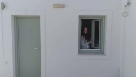 Vista-aérea-de-la-ventana-de-apertura-de-la-mujer-en-casas-blancas-tradicionales,-Grecia.