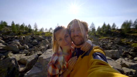 Hikers,-couple--taking-selfie-portrait-on-mountain-trail.-sun-shining-over-the-mountains.-Beautiful-sunbeam-effect-making-an-idyllic-landscape.-Young-couple-hiking-take-video-selfie-in-Switzerland