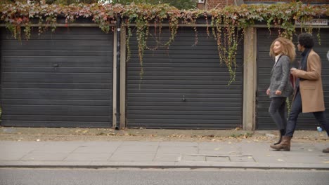 Stylish-Young-Couple-Walking-Past-Garages-On-City-Street