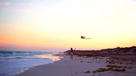 Little-running-girl-with-flying-kite-on-tropical-beach-at-sunset.-Kids-play-on-ocean-shore.-Child-with-beach-toys.