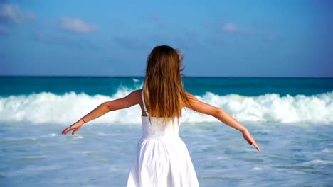 Liebenswert-glückliches-kleines-Mädchen-auf-weißen-Strand-mit-Blick-auf-den-Ozean.-Laut-Meer-und-einem-kleinen-niedlichen-Kind