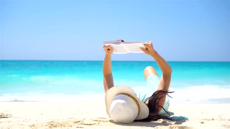 Mujer-joven-s\'está-leyendo-en-tropical-playa-blanca