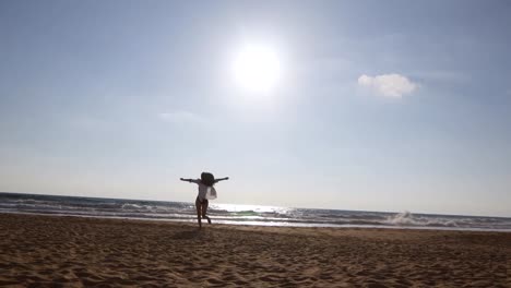 Junge-Frau-am-Strand-zum-Meer-bei-Sonnenuntergang-und-erhobenen-Händen-ausgeführt.-Schöne-junge-Mädchen-am-Sandstrand-gehen-Sie-zum-Strand-und-genießen-die-Freiheit-im-Urlaub.-Entspannen-Sie-im-Sommerurlaub.-Rückseitige-Ansicht-von-hinten