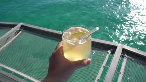 Hand-holding-yellow-bright-summer-tropical-cocktail-with-beautiful-tropical-ocean