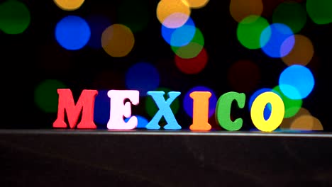 Colorful-word-"Mexico"-from-multi-colored-wooden-letters-in-front-of-abstract-blurred-lights-bokeh-background