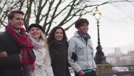 Friends-Walking-Along-South-Bank-On-Winter-Visit-To-London