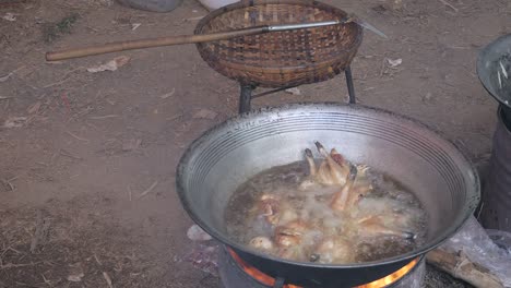 Deep-frying-chickens-in-a-large-wok-cooking-on-a-charcoal-and-wood-brazier-stove-outdoors