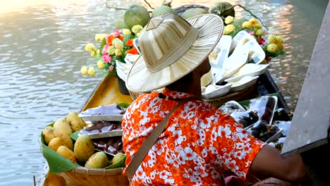 Seller-of-exotic-fruits-on-a-boat-and-a-straw-hat-sails-on-the-river-in-Thailand,-on-a-floating-market,-Pattaya