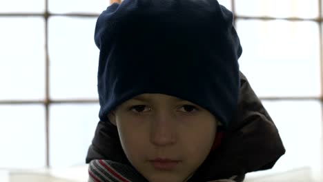 portrait-of-offended-boy-stands-alone-near-a-broken-window,-looking-into-the-camera