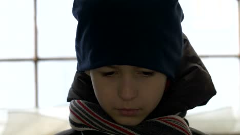 portrait-of-unhappy-boy-stands-alone-near-a-broken-window,-looking-into-the-camera,-cold-weather