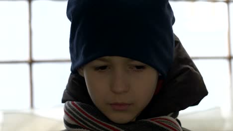 portrait-of-offended-boy-stands-alone-near-a-broken-window,-looking-into-the-camera