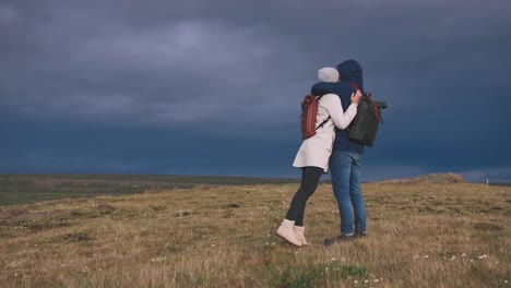 Young-loving-couple-hugging-in-field-on-background-of-epic-dramatic-clouds,-slow-motion