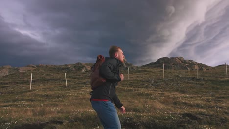 Young-man-walking-in-field-way-to-mountains-with-dramatic-sky-background,-slow-motion