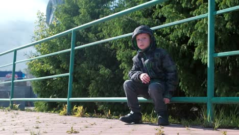 Niño-de-siete-años-sentado-en-una-valla-en-el-parque-y-mira-alrededor.