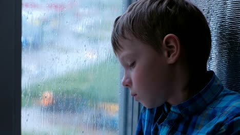 Boy-looks-out-the-window-in-the-rain-and-is-sad.