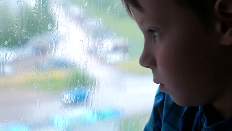 Boy-looks-out-the-window-in-the-rain-and-is-sad.