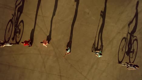 Teenagers-riding-in-row-on-bikes,-roller-skates-and-scooters-cast-long-shadows.-Top-view