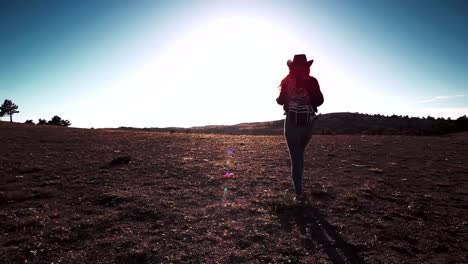 Silueta-de-mujer-con-sombrero-con-mochila-caminando-por-el-campo-al-atardecer-delgado-deportes