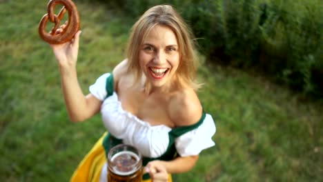 Festival-Oktoberfest.-Eine-Frau-in-einem-bayerischen-Anzug-mit-einem-großen-Glas-Bier-und-eine-Brezel-in-ihren-Händen-fröhlich-lacht-und-schaut-in-die-Kamera.-Ansicht-von-oben