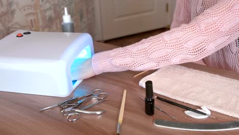 Woman-dries-her-nails-with-shellac-in-UV-lamp-and-browsing-internet-in-mobile-phone.-Close-up-hand.