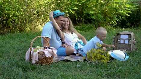 La-familia-tenía-un-picnic-en-la-naturaleza.-Mamá,-papá-y-pequeño-hijo-divirtiéndose-y-jugando-con-los-sombreros-en-la-hierba-en-el-parque.