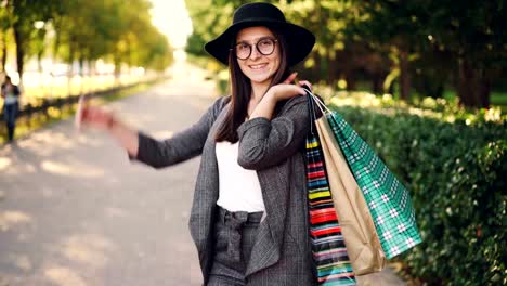Portrait-of-pretty-young-woman-holding-paper-bags-standing-outdoors-in-the-city-and-looking-at-camera-on-sunny-autumn-day.-Shopping,-youth-and-street-concept.
