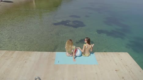 Aerial-view-of-two-women-sits-on-wooden-deck-in-Panagopoula,-Greece.