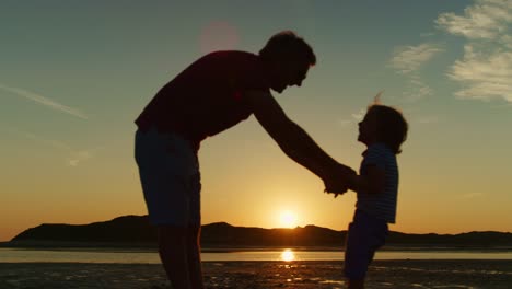 Silhouette-von-Vater-und-Sohn-spielen-zusammen-am-Strand.