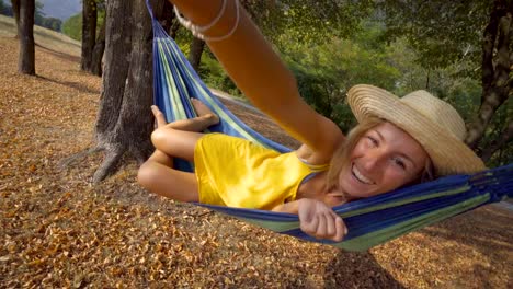 Young-woman-taking-selfie-on-hammock-relaxing-at-sunset-in-Autumn--People-travel-vacations-technology-communication-concept