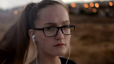 Teenage-girl-with-eyeglasses-listening-to-the-music-on-sunset,-close-up