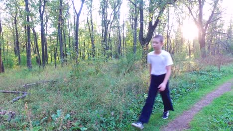 Slim-teen-boy-goes-along-a-path-in-the-forest.-The-boy-finished-the-training-and-goes-away-home.-Sports-in-nature.-Morning-sun-forest-at-dawn.