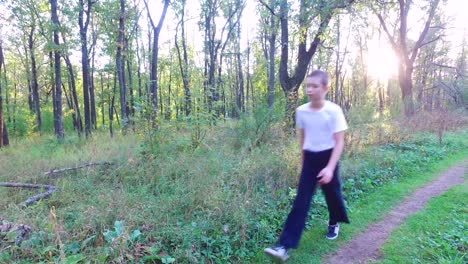 El-niño-adolescente-delgado-va-por-un-camino-en-el-bosque.-El-chico-terminó-el-entrenamiento-y-se-va-a-casa.-Deportes-en-la-naturaleza.-Bosque-de-sol-de-la-mañana-al-amanecer.