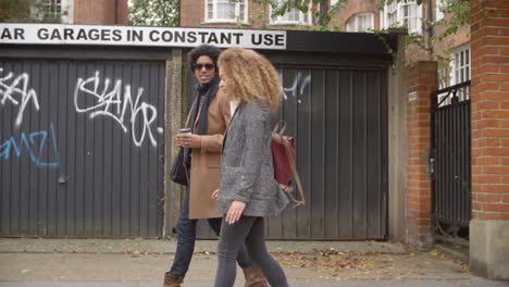 Stylish-Young-Couple-Walking-Past-Garages-On-City-Street