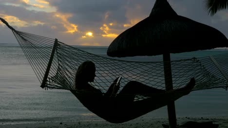 Frau-mit-Telefon-liegen-in-der-Hängematte-am-Strand