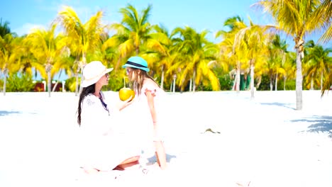 Little-kid-and-young-mom-with-coconut-milk-on-exotic-beach.-Cute-girl-drinks-healthy-milk-from-coconut-in-a-palm-grove