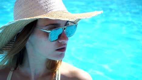 girl-with-glasses-and-hat-looks-toward-near-blue-pool-close-up