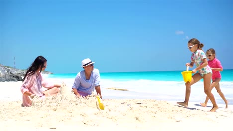 Family-of-four-making-sand-castle-at-tropical-beach