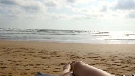 Female-feet-playing-against-the-sea.-Legs-of-beautiful-young-woman-relaxing-on-sea-shore-during-summer-vacation-travel.-Point-of-view-of-sexy-girl-lying-and-tanning-on-the-beach.-Close-up