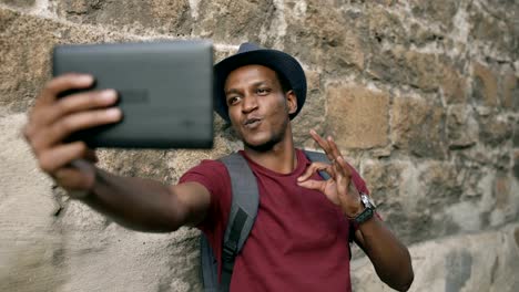 Happy-african-american-tourist-man-having-online-video-chat-using-tablet-computer-while-travelling-in-Europe