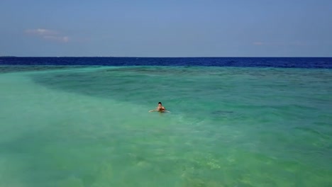 Die-Luftbild-Drohne-Kamera-fliegt-um-paar-Schwimmen-im-Indischen-Ozean-auf-einem-leeren-Strand.-Aufnahmen-der-beiden-Liebenden-auf-Hochzeitsreise-Baden-und-küssen-im-smaragdgrünen-Meer-von-oben